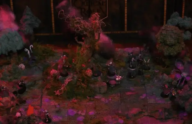An animated GIF showing scenes of a battlemap of a forest clearing with a large leafless Hawthorn tree near the center, bathed in an eerie red glow. Fake smoke rises from that tree and others at the edges of the map. Orange lights indicate that the trees are on fire. Thimble, Kattigan, Wulferic, Vaelus, Occtis, Pin, and Ulbid Morn stand near the tree. A number of Candescent Creed members and fairy poachers are scattered around the area, especially at the base of the Hawthorn tree. A small animal hide hut is at the edge of the battlemap. Large red mushrooms with white spots and a huge purple flower with long fibers emerging from it are at the other end near a lake.
