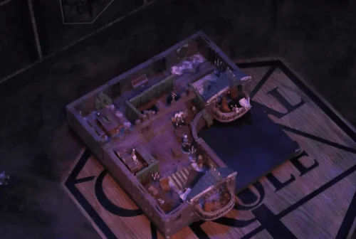 An animated GIF showing scenes of a battlemap of VIP box seats in a theater. An enclosed space with two balconies on one side of it, the right one further back than the left one. Wicander sits at a small round table across from Godard Halovar. Lioran and Iris Halovar are seated on cushioned red chairs on the right balcony, while the chairs on the left balcony are empty. Inside is a bar with a bartender behind the counter, some table seating, and green curtains closing off a small section at the back.