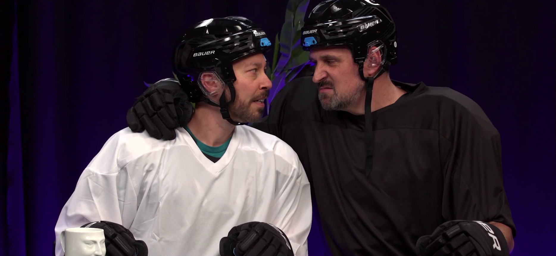 Sam and Travis at the Critical Role Announcement Playhouse table, dressed in hockey outfits and staring into each other’s eyes, their faces less than a foot apart. Sam looks frightened, but tantalized. Travis scowls in a sexy way. Travis’s arm is around Sam’s shoulder.