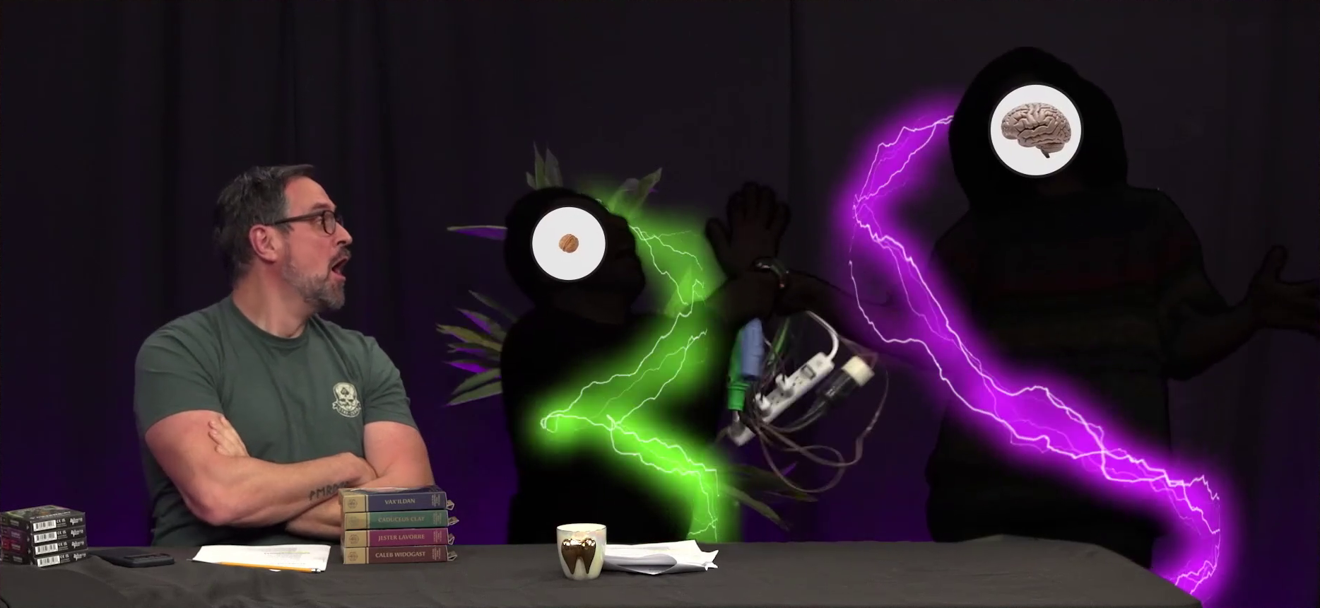 The Critical Role Announcement Playhouse table. Silhouettes of Sam and Quyen have green and purple lightning surrounding them as they both hold on to an overloaded powerstrip. A white circle in Sam’s head shows a walnut where his brain should be, while in Quyen’s head it shows an actual brain. Travis looks on, aghast. On the table in front of them are four cardboard dice boxes labeled “VAX’ILDAN”, “CADUCEUS CLAY”, “JESTER LAVORRE”, and “CALEB WIDOGAST”.