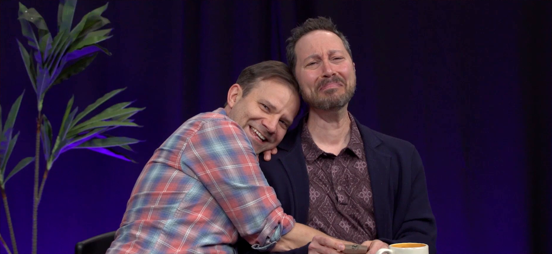 Liam and Sam at the Critical Role Announcement Playhouse table. Liam holds Sam possessively, his right arm wrapping around near his waist and his left hand on his shoulder. He looks directly into the camera with a creepy expression on his face. Sam looks extremely uncomfortable but seems unwilling to move from his position.