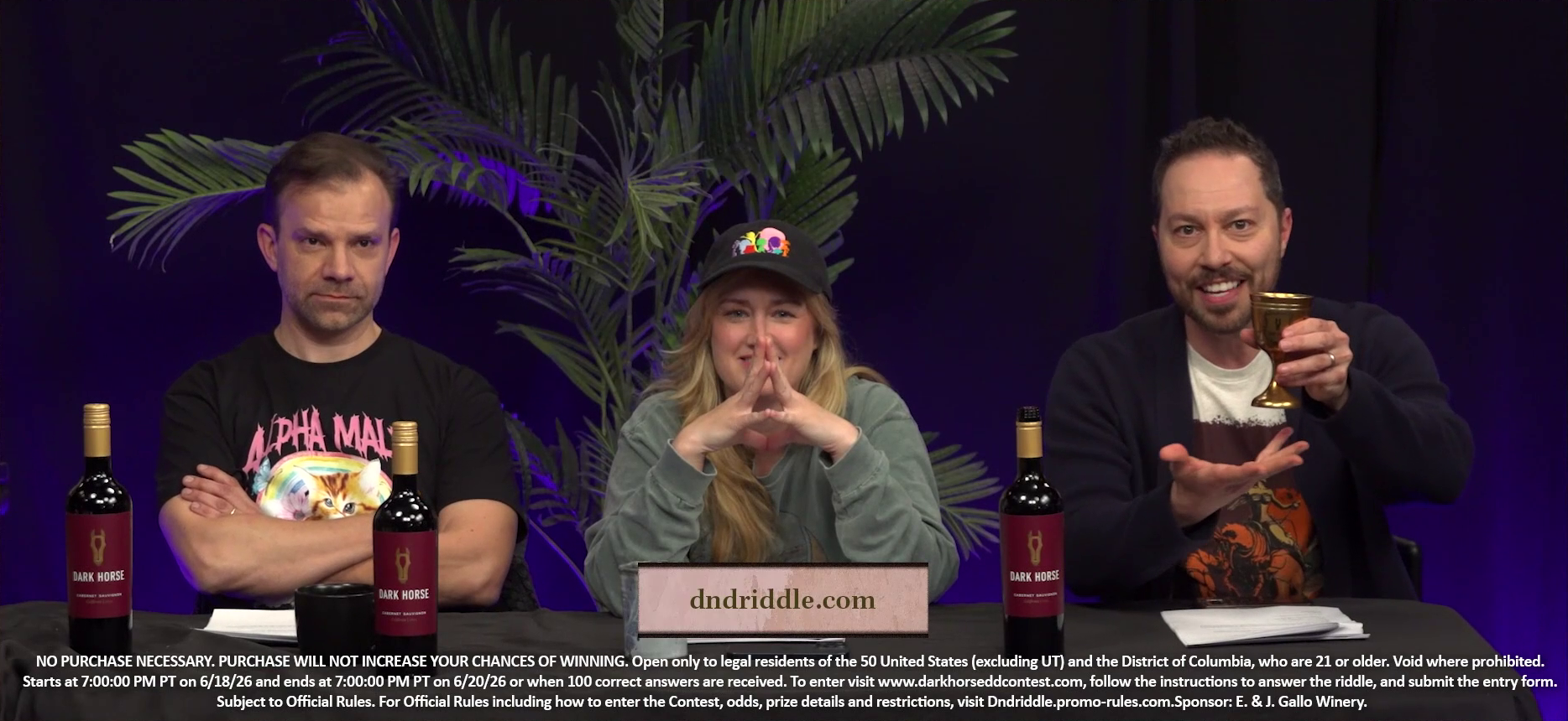 Liam, Ashley, and Sam sit at the Critical Role Announcement Playhouse table. Sam holds up a golden wine glass, gesturing to it his with right hand. Three bottles of red Dark Horse wine are on the table. Text on screen reads “dndriddle.com”. Underneath it is text specifying the fine print of the Dark Horse riddle contest, which ran from 6/18/2026 to 6/20/2026. Ashley smiles with her fingers steepled in front of her. Liam crosses his arms, frowing.