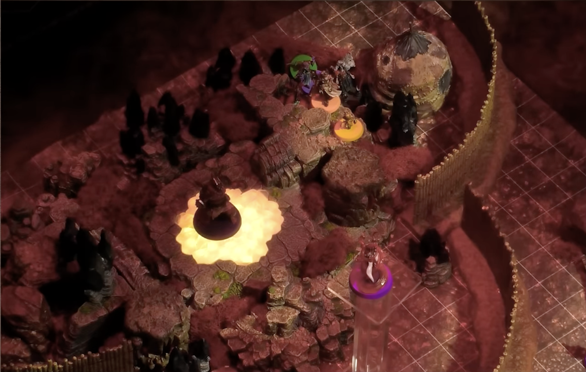A battlemap of a fenced encampment built around a glowing portal on the ground. A large Reiloran stands on the portal while another flies above in the foreground. The party stands by a patchwork hut separated from the large Reiloran by some stone formations.