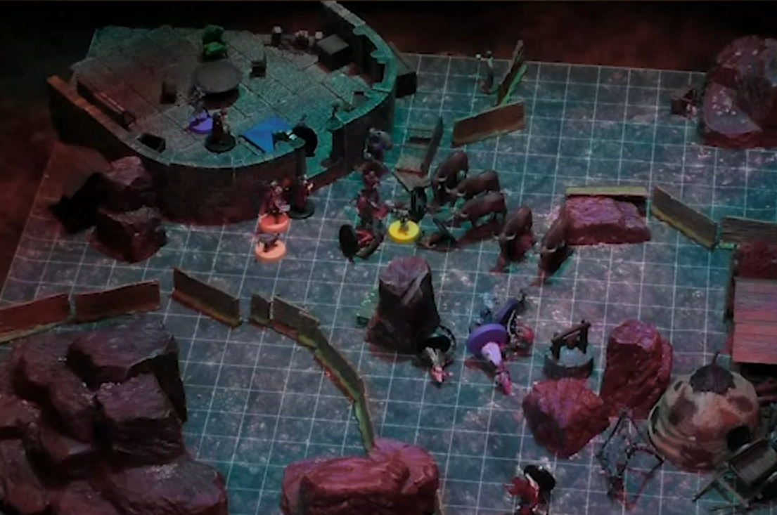 A battlemap of a rounded stone building with an expanse of flat ground outside. A purple token and a number of red-caped individuals are toppled outside and surrounded by cow-like livestock.