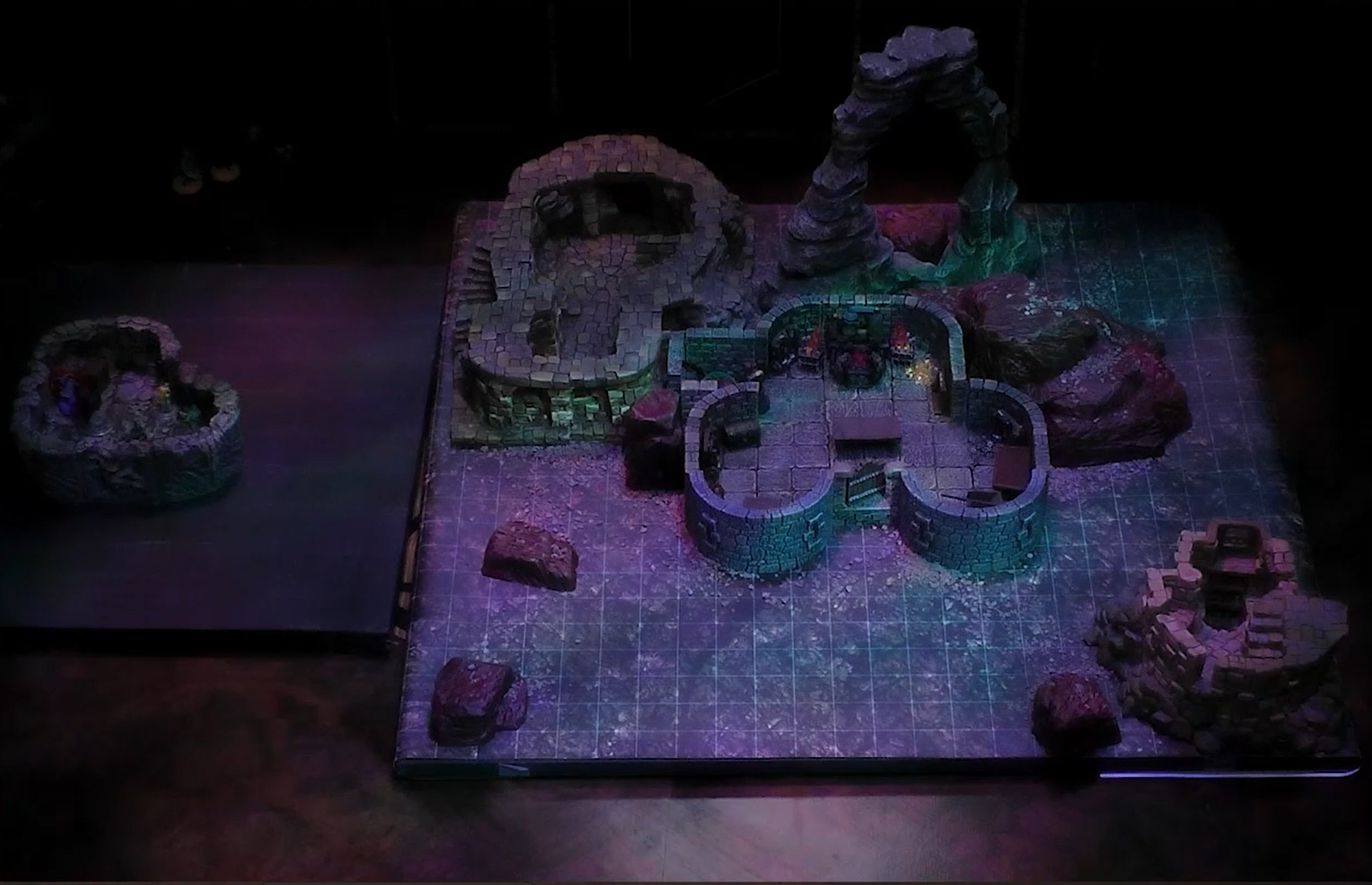 A battlemap of a stone building containing a forge. Another room with more haphazard stonework that doesn’t seem connected is off to the side. A stone archway is also near the building. A small stone basement is placed off the battlemap some distance away.