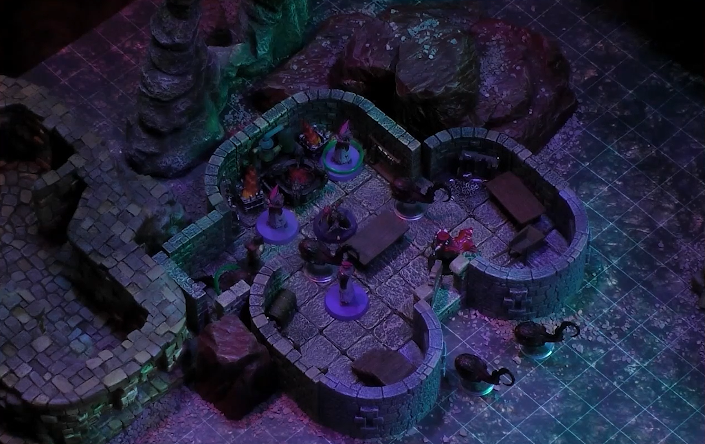 A battlemap of a stone building containing a forge. Two Reilorans, one of which has a green ring around it, are by the forge. Another Reiloran and a red-caped individual are near the entance. Three Slithers are in the building, and two are outside.