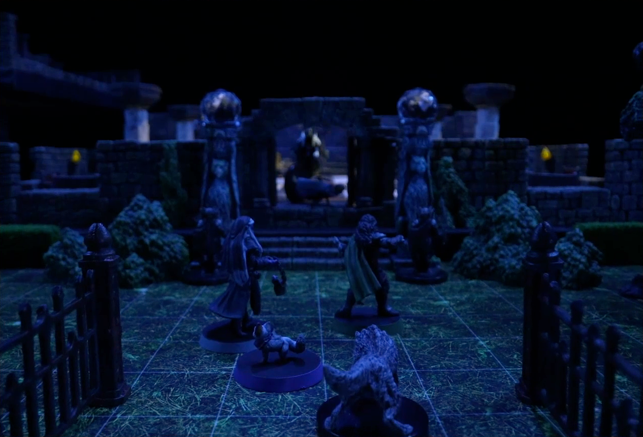 A battlemap of a stone palace focused on the entrance. Vaelus, Julien, Pincushion, and Thaisha in wolf form stand just inside the gate. Two stone pillars bearing carvings of griffins and topped with large spherical crystals frame the entryway to the palace. In the background, Primus Tachonis stands in the entryway over a fallen guard.