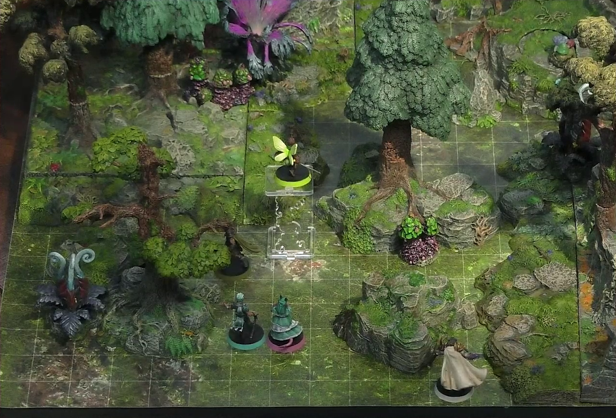 A battlemap of a forested glade with a variety of trees, mushrooms, and fey-like, purple plants. Thimble flies 10 feet in the air near a tree with Kattigan below her, while Wicander and Tyranny stand next to each other nearby. Teor stands just behind a nearby rocky outcropping. A large purple flower with four petals is in the background.