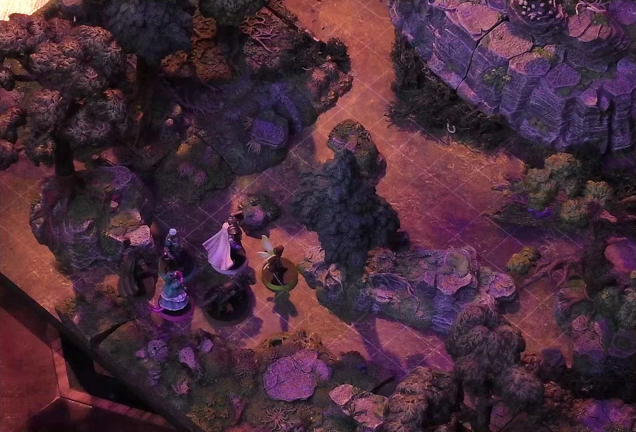 A battlemap of a sparse forested space focused on Kattigan, Wicander, Teor, Thimble, Wulferic, and Tyranny looking towards a large rocky mound. A small wooden structure covered in skulls is visible just at the edge of the mound.