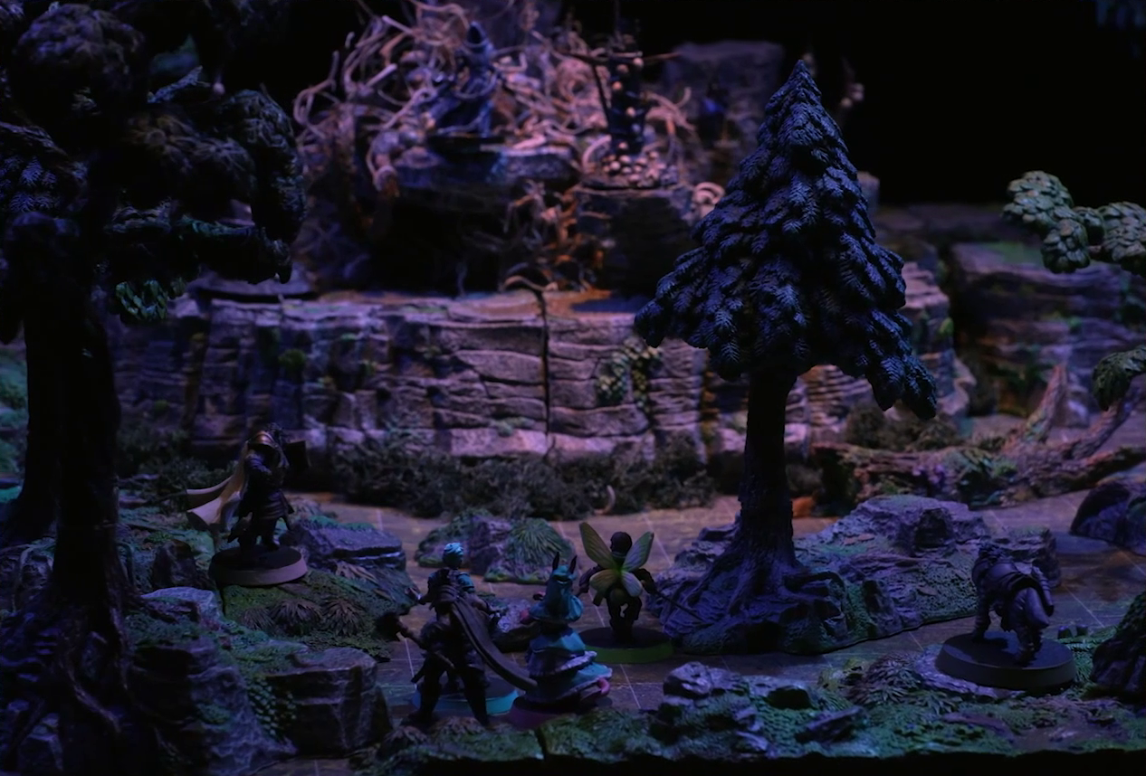 A battlemap of the Wraith Tree on a large rocky mound in a sparse forested space. Kattigan, Wicander, Teor, Thimble, Wulferic, and Tyranny look towards the tree. A black-cloaked specter stands at the base of the tree, blurry in the background. Wooden structures covered in skulls surround the tree.