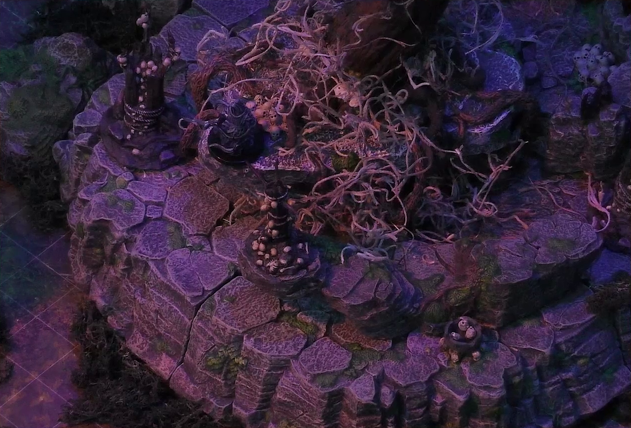 A battlemap of the Wraith Tree on a large rocky mound in a sparse forested space. A black-cloaked specter stands at the base of the tree. The Wraith Tree has thin, white, spaghetti-like tendrils hanging from its bare branches. Wooden structures covered in skulls surround the tree.