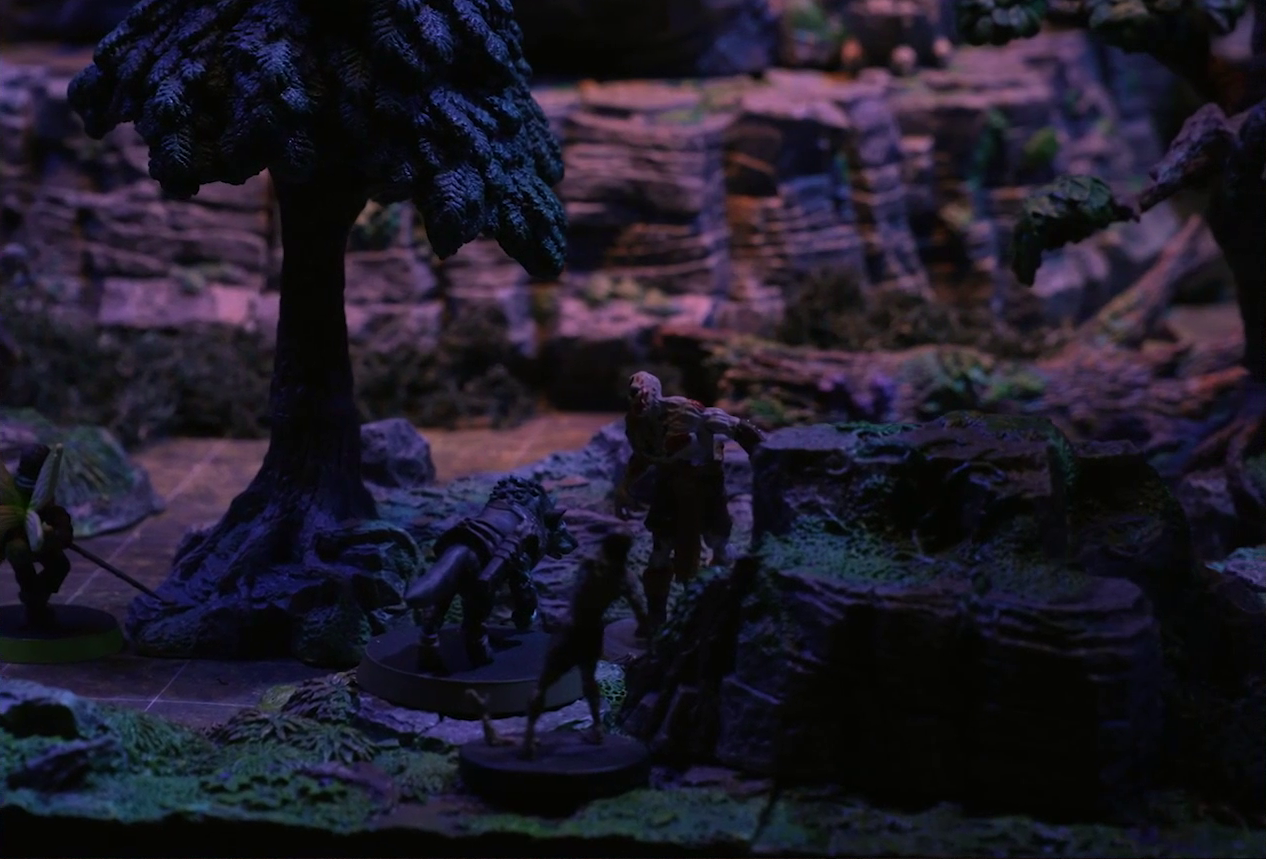 A battlemap of a sparse forested space focused on Wulferic facing off against two zombies, one large and burly, the other thin and spindly. Thimble stands just at the left edge of the image. The base of a large rocky mound is visible in the background.