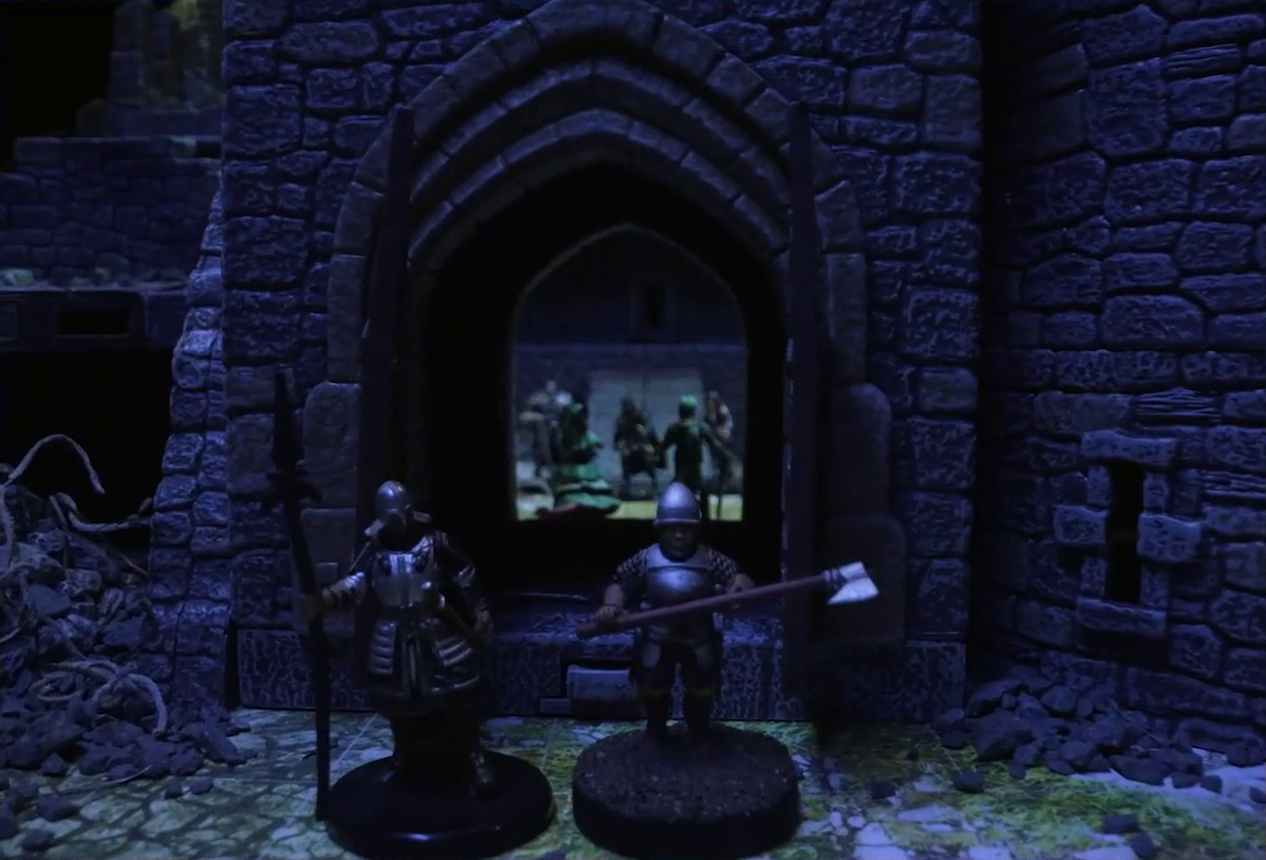 A battlemap of a stone castle focused on two guards at the open entry door into the courtyard. Beyond the entrance, Tyranny, Wicander, and some other individuals are blurrily visible. The tower to the right of the entrance has collapsed, thin tangled tree roots emerging from the rubble.
