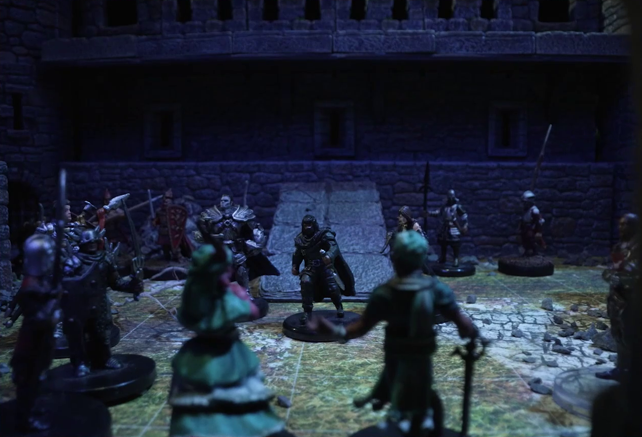 A battlemap of a stone castle courtyard focused on Tyranny and Wicander standing in a circle with a number of armored knights. Casimir, dressed in black with a cape and holding a dagger point down, stands across from Tyranny and Wicander. Some rubble is on the ground and a raised walkway is visible at the top of the back wall.