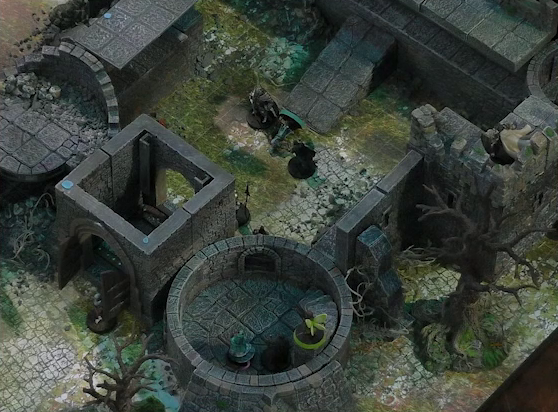 A battlemap of a ruined stone castle with sparse dead trees around its edges. The walled courtyard has a tower at each corner. The bottom-left tower has collapsed. Teor stands on the right wall overlooking the courtyard. Tyranny and Casimir stand in the bottom right tower, with Thimble standing at the top of the stairs in that room. Inside the courtyard are some armored individuals standing over a fallen Wicander. One guard stands in front of the open wooden entry door into the courtyard.