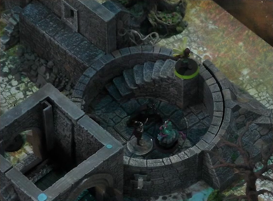 A battlemap of a ruined stone castle focused on the interior of small circular tower room. Tyranny faces off against a knight, while Casimir lays on the ground next to them. Thimble stands at the top of the stairs curving around the exterior of the room.