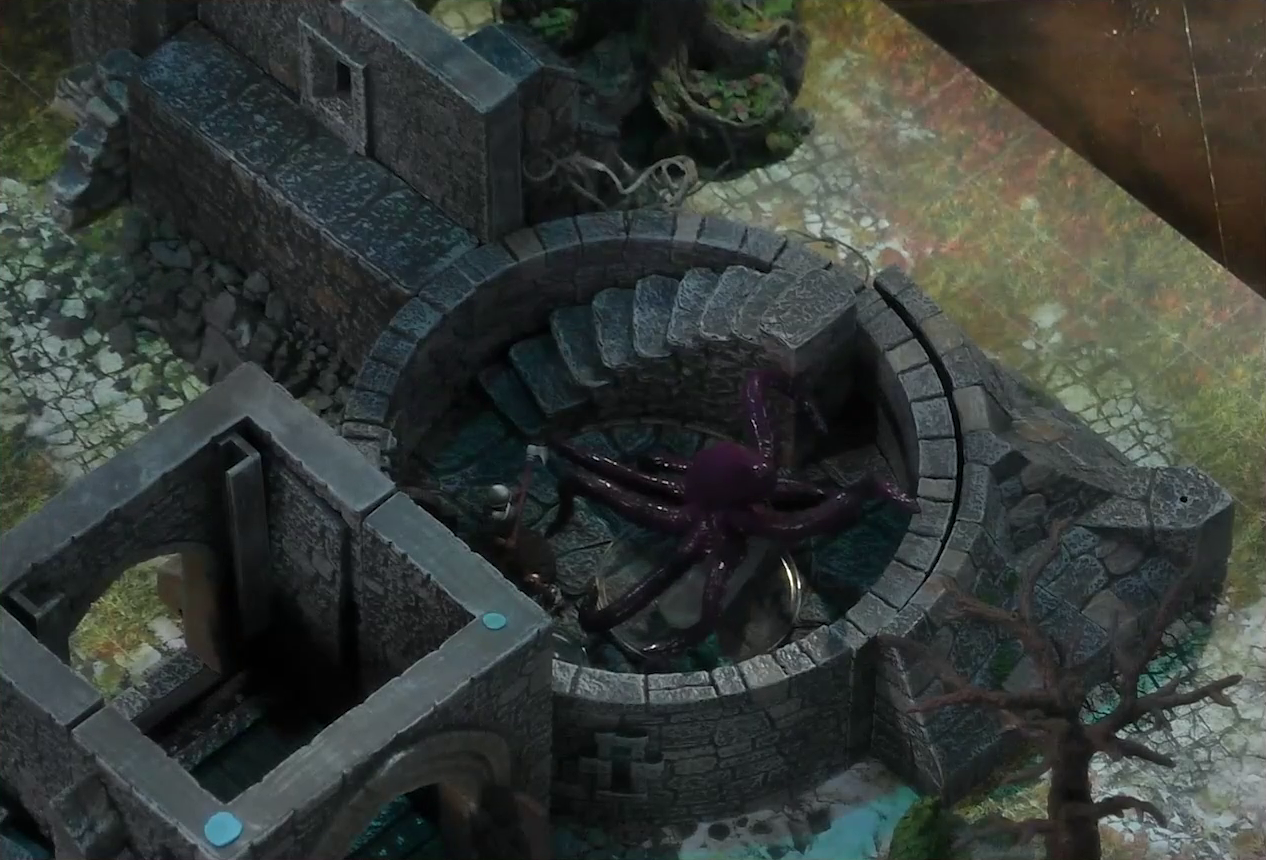 A battlemap of a ruined stone castle focused on a giant red squid in the interior of a small circular tower room. An armored soldier wielding a long axe faces off against the creature. A staircase curves up along the edge of the room. Tyranny is just visible to the squid’s side. The open wooden entry door to the castle courtyard is next to the tower.