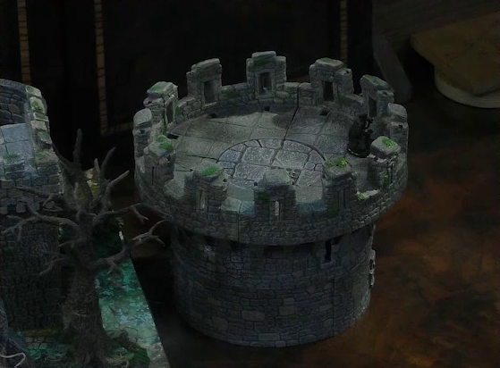 A battlemap of a stone parapet tower. Casimir, dressed in black, stands at the top of the tower, near the edge. The tower is placed off to the side of a larger battlemap with a castle wall and a leafless tree visible.
