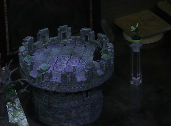A battlemap of a stone parapet tower. Thimble flies a short distance from the tower, slightly above its top. Casimir, dressed in black with a cape, stands at the top of the tower, near the edge. The tower is placed off to the side of a larger battlemap with a leafless tree visible. Some coasters and a DM screen are visible in the background.