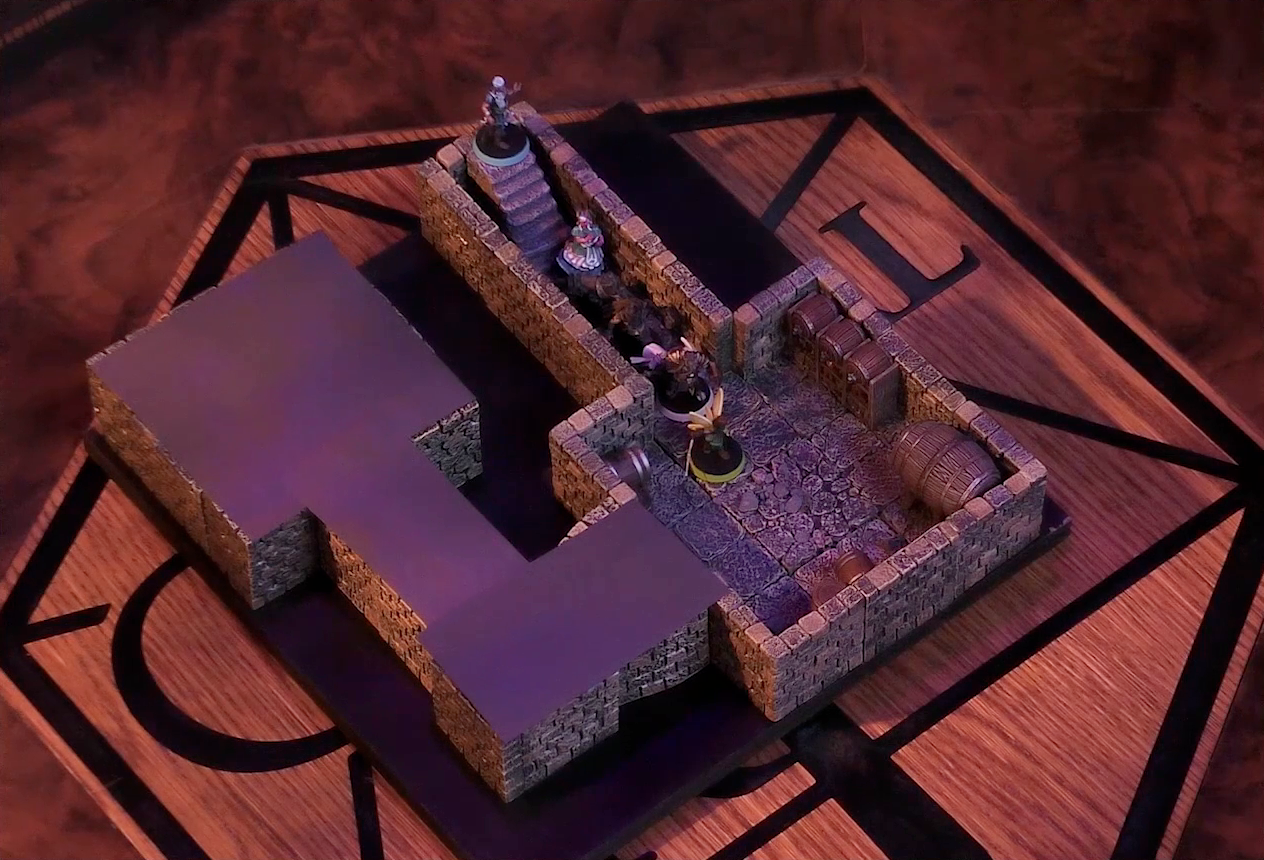 A battlemap of a small stone dungeon. A short set of stairs go down into a hallway which leads to a chamber containing some barrels against the walls. Wicander, Tyranny, Wulferic, Kattigan, Teor, and Thimble are in single file down this hallway, with Wicander at the top of the stairs and Thimble in the barrel chamber. Another hallway leads off and turns a corner into a second chamber. Both this final hallway and chamber are obscured with black construction paper.