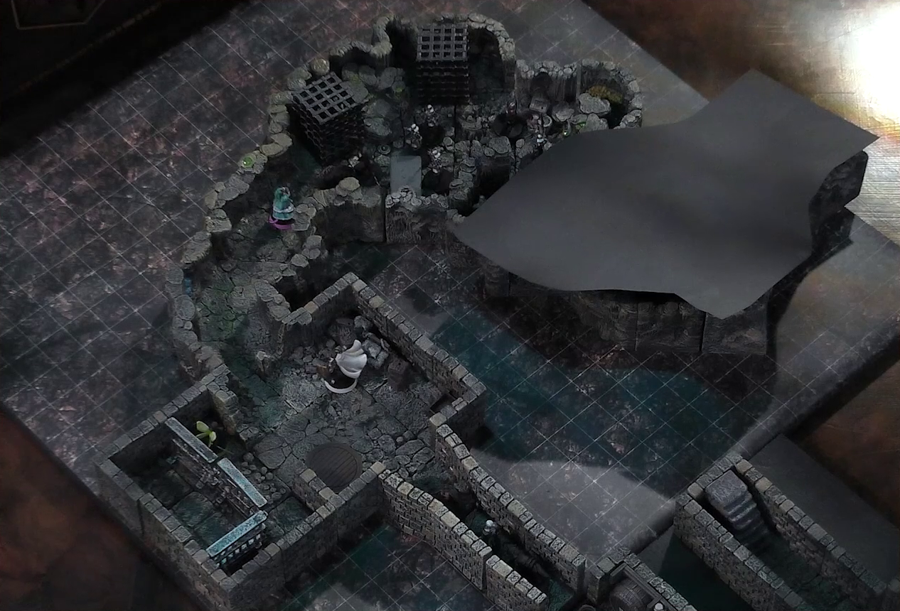 A battlemap of a stone dungeon. Wulferic, Wicander, and Kattigan stand single-file in a narrow hallway leading into a chamber. In that chamber, Thimble stands near metal bars resembling an empty jail cell against another wall. Teor is across the room in the corner with some wooden containers. Deeper into the dungeon is a naturally-formed chamber, where Tyranny faces off against a basilisk, a black-cloaked knight, and five armored guards with spears. Two large black cube-shaped cages are against one wall, and a stone slab with a coil of rope on it is against the opposite wall. The area deeper into the dungeon is obscured by black construction paper. Small glowing green dots and turquoise mushrooms are scattered across the floor and walls.
