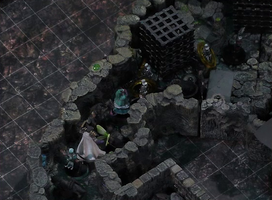 A battlemap of a naturally-formed small stone dungeon chamber. Wulferic, Wicander, Teor, Thimble, Kattigan, and Tyranny face off against a basilisk, a black-cloaked knight, and three armored guards. The guards have yellow status rings around them. Two large black cube-shaped cages are against one wall, and a stone slab with a coil of rope on it is against the opposite wall. Small glowing green dots and turquoise mushrooms are scattered across the floor and walls.