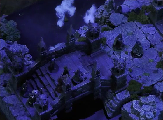 A battlemap of an ornate stone bridge over water. Vaelus, Occtis, Aranessa, and Thaisha stand at one end, with Julien and Enmity further ahead down some steps. Behind them all at the edge of the bridge are two druids. White foam caps waves in the water below.
