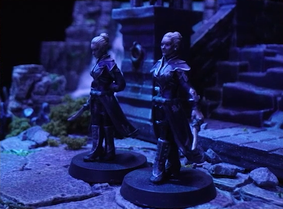 A battlemap of an ornate stone bridge focused on Petra and Ryah Tachonis standing side-by-side. They both wear light metal armor, cloaks, and knee-length boots, and wield daggers in opposite hands. Their hair is white and done up in a bun on top of their heads. Behind them some stairs rise along the bridge.