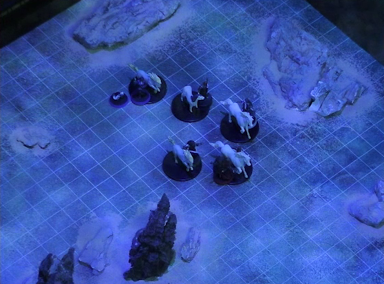 A battlemap of a flat, sandy expanse under the cover of night. Occtis, Pin, Gaya Seremai, Vaelus, Thaisha, and Julien stand in a rough line with their five white horses. Thaisha is in front, with Julien and Vaelus behind, followed by Gaya and then Occtis. Some jagged rocky formations jut from the otherwise empty landscape.