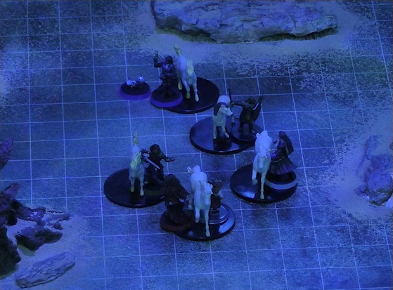 A battlemap of a flat, sandy expanse under the cover of night. Occtis, Pin, Gaya Seremai, Vaelus, Thaisha, and Julien stand in a rough line with their five white horses. Thaisha is in front, with Julien and Vaelus behind, followed by Gaya and then Occtis. Some jagged rocky formations jut from the otherwise empty landscape.