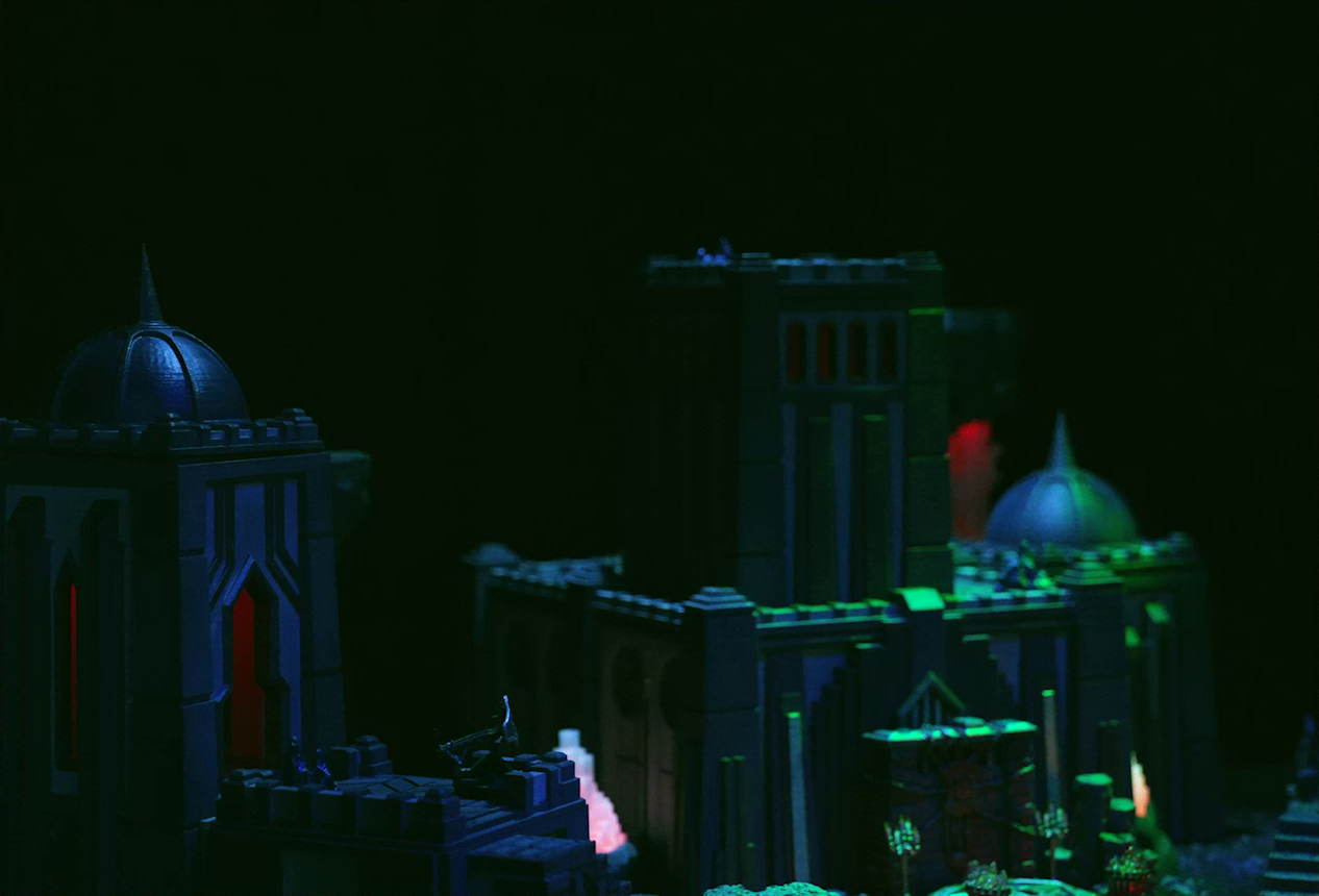 A battlemap of a couple towers under cover of night. The left tower has a dome roof with a spike emerging from its center. On a platform jutting from the tower is a ballista. In front of the tower to its right is a metal sacrificial platform with two candelabras at its corners. Two red glowing crystal pillars sit between the towers.