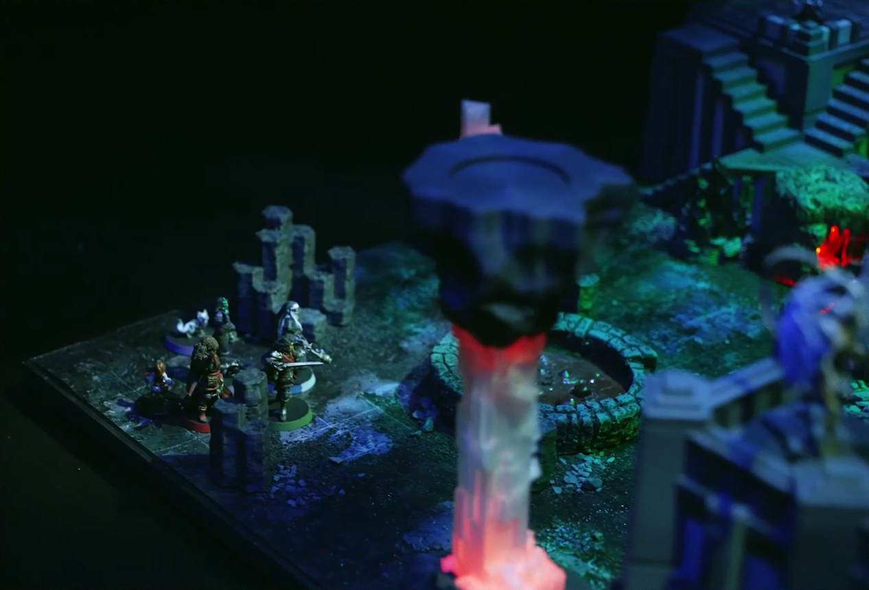 A battlemap of a walled courtyard under cover of night focused on Pin, Vaelus, Occtis, Dr. Talter, Thaisha, and Julien standing near a circular pool of dark red blood. A red glowing crystal pillar is in the foreground, and next to it on top of a stone wall is the white-winged and scorpion-tailed Tertia Tachonis. In the background, stairs lead up a tower to a platform with a ballista on it.