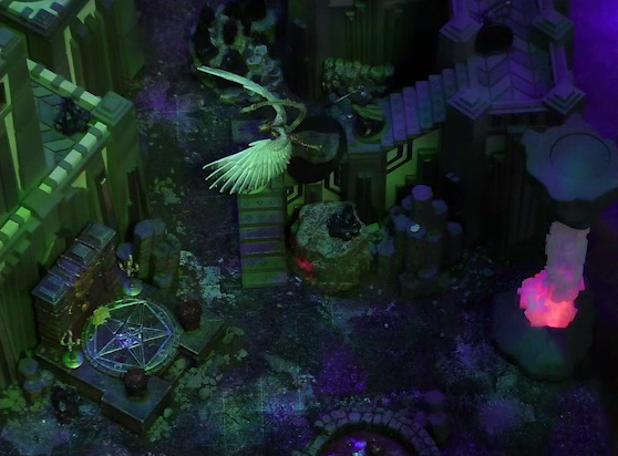 A battlemap of a walled courtyard under cover of night. The white-winged and scorpion-tailed Tertia Tachonis descends a flight of stone stairs pursued by Julien. At the base of the stairs is a metal sacrificial platform bearing a pentagram. A tower rises above the platform. To the side is a red glowing crystal pillar. At the bottom of the image is a circular pool of dark red blood.