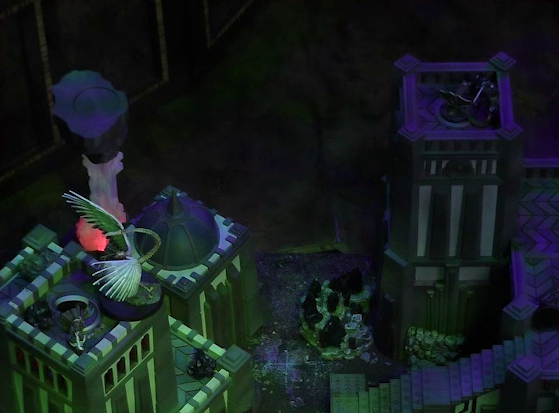 A battlemap of a walled courtyard under cover of night. The white-winged and scorpion-tailed Tertia Tachonis stands at the top of a tower over the body of Vaelus. Julien stands on top of a tower next to it, pointing a ballista at Tertia. A red glowing crystal pillar stands behind Tertia’s tower.