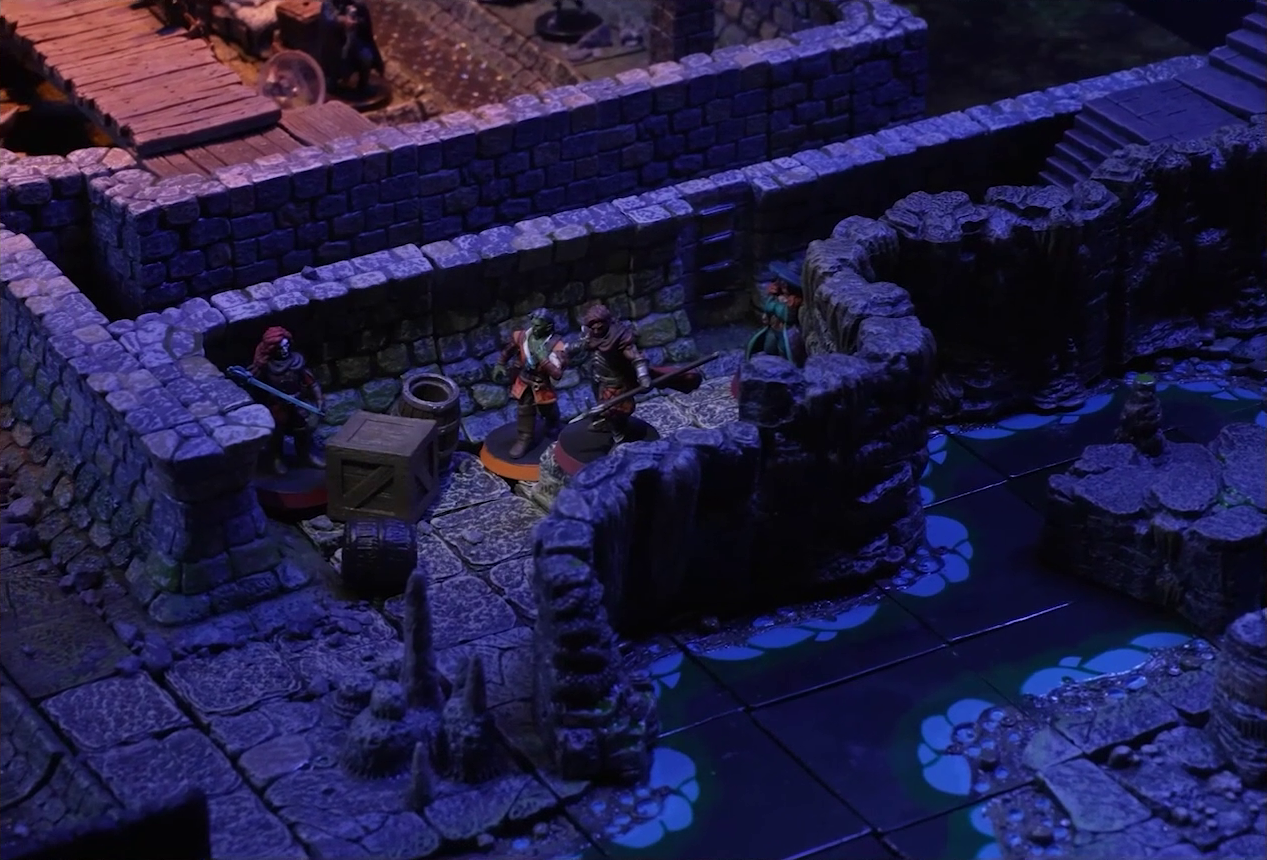 A battlemap of a stone underground area in the sewer. Bolaire, Halandil, Azune, and Murray stand in a hallway which runs beside an underground river. A flight of stairs leads down into the hallway. Off the hallway is a room, where two Crow Keepers and a fallen Demodus Blix are visible.