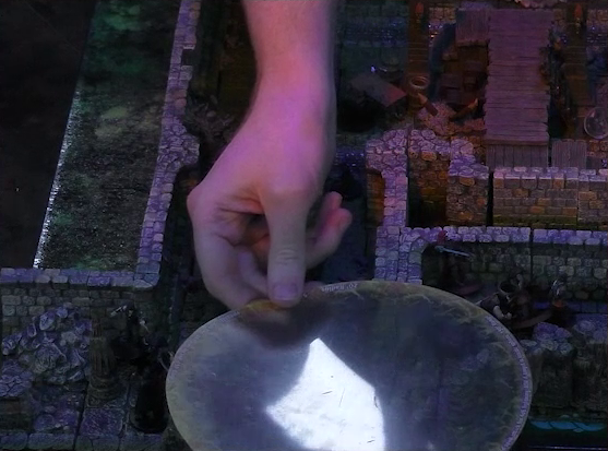 A battlemap of a stone underground room in the sewer. Brennan holds a transparent area of effect circle over a section of hallway outside the room. A couple Crow Keepers, Azune, and Halandil are out of the area of the circle.