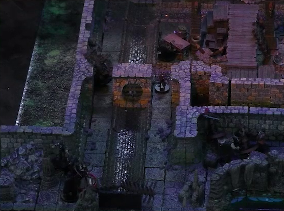 A battlemap of a stone underground room in the sewer. Bolaire, Azune, Halandil, and Murray fight Crow Keepers in a hallway around the corner from the room. One Crow Keeper guards the south entrance to the room. A sewer trench runs in a circle in the room and exits through both entrances. A raised wooden boardwalk goes from the wall to the center of the room among wooden boxes and three stone pillars holding up the ceiling.