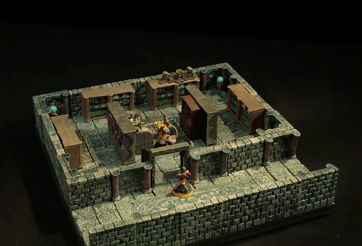 A small battlemap of a library chamber. Halandil stands in the open doorway to the library, looking in at a Nama. The library is filled with bookshelves and one desk cluttered with books and trinkets. The Nama stands next to the desk.