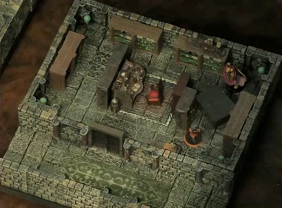 A small battlemap of a library chamber. Halandil stands on one end of a fallen bookcase, with a Nama on the other side. The Nama has a “CONCENTRATION” status ring around his miniature. The library is filled with bookshelves and one desk cluttered with books and trinkets. In front of the desk is a red padded chair.