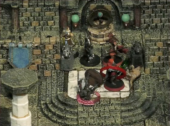 A battlemap of a large stone banquet chamber with surrounding hallways. Bolaire, Azune, and a Timmonish knight face off against two assassins entering the chamber through its north entrance. A fallen Hound of the King with a “POISONED” status ring around its miniature lays on the ground just inside the entrance. Bolaire has a red status ring around his miniature, and a downed assassin has a “CONCENTRATION” status ring.