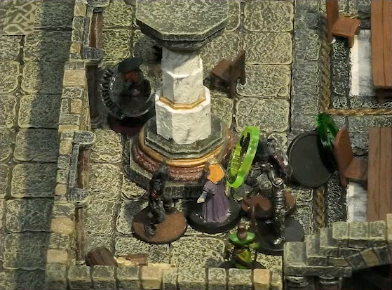 A battlemap of a large stone banquet chamber with surrounding hallways. King Augustus Valian and a druid face off against three assassins. One of the assassins has a gree status ring around its miniature. Murray hides invisibly behind a nearby pillar. A downed Hound with a “POISONED” status ring is nearby.