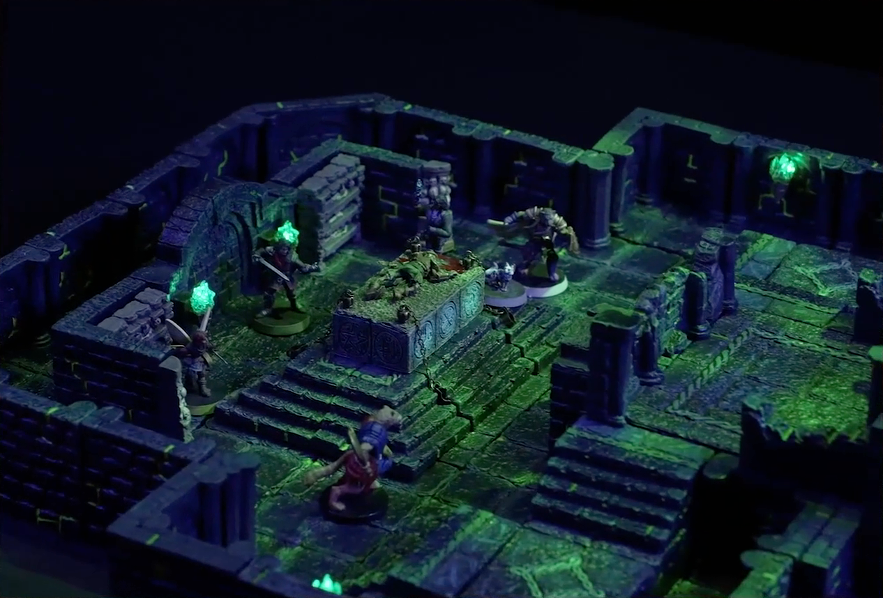A battlemap of a stone chamber. A stone altar is in the center with a skeletal corpse on top of it, next to which stand Occtis and Pincushion. Around the altar are Thimble, Julien, Teor, and Talcydimir. Behind the altar is a circular hole leading into the wall. Two staircases on either side of the hole lead up to a door with a portcullis. The room is lit by a sickly green glow emanating from torches on the walls.