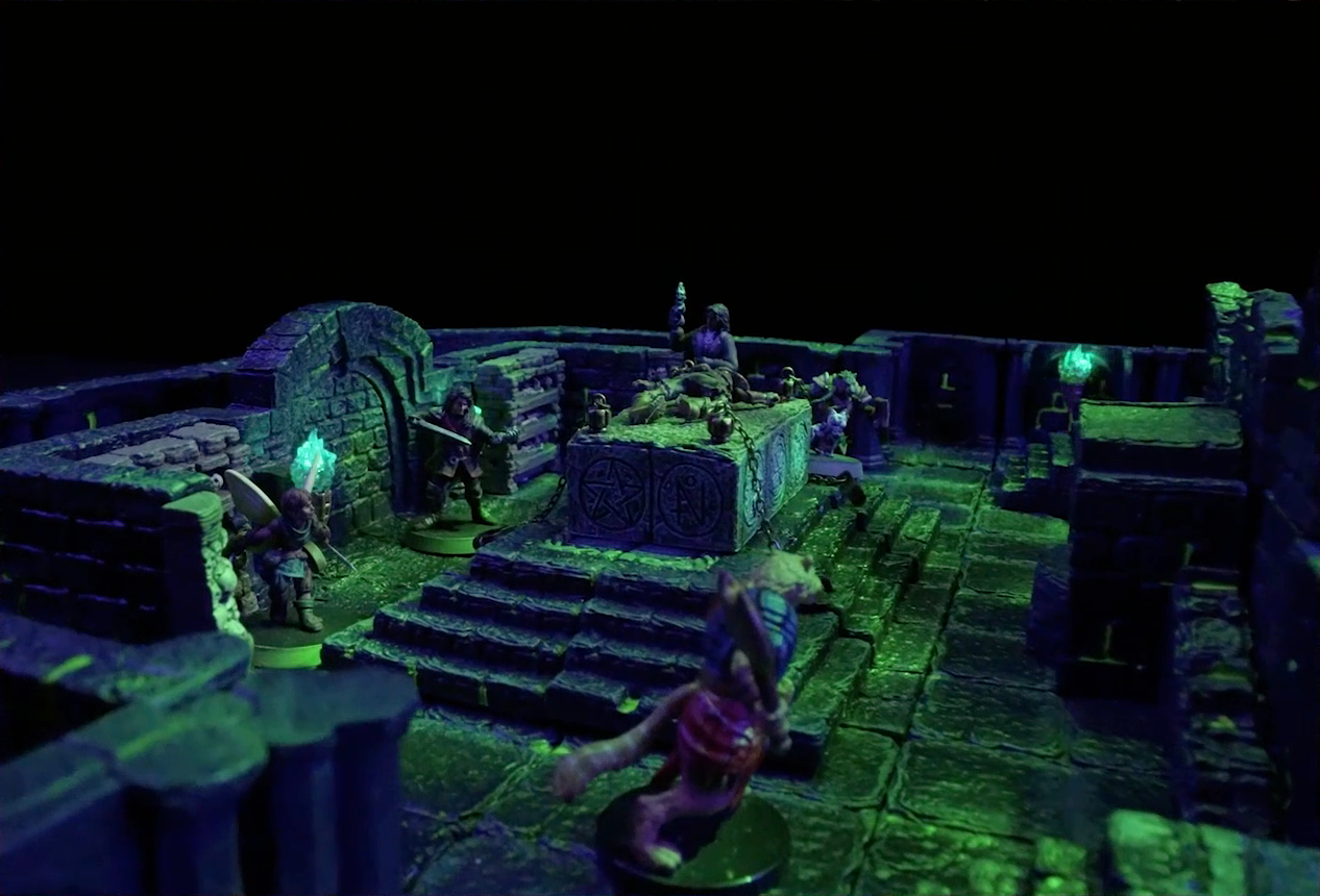 A battlemap of a stone chamber. A stone altar is in the center with a skeletal corpse on top of it, next to which stand Occtis and Pincushion. Around the altar are Thimble, Julien, Teor, and Talcydimir. Behind the altar is a circular hole leading into the wall. Two staircases on either side of the hole lead up to a door with a portcullis. The room is lit by a sickly green glow emanating from torches on the walls.