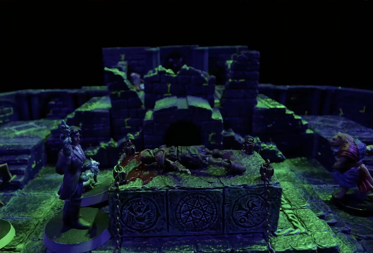 A battlemap of a stone chamber. Occtis stands over a stone altar on which is a bleeding skeletal corpse. Pincushion stands beside Occtis. On the other side of the altar is Talcydimir. Chains hang off each of the four corners of the altar, and on its side are three circular glyphic symbols. Behind the altar is a circular hole leading into the wall. Two staircases on either side of the hole lead up to a door with a portcullis. The room is lit by a sickly green glow emanating from torches on the walls.