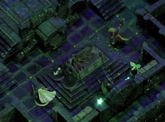 A battlemap of a stone chamber. A stone altar is in the center with a skeletal corpse on top of it, next to which stand Occtis and Pincushion. Around the altar are Thimble, Julien, Teor, and Talcydimir. Behind the altar is a circular hole leading into the wall. The room is lit by a sickly green glow emanating from torches on the walls.