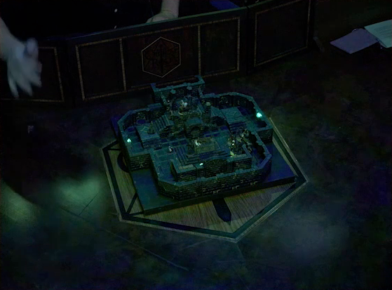 A zoomed-out view of a battlemap of a stone chamber on the Critical Role table. Brennan’s hand reaches out from behind his DM screen to roll a d4 next to the map. A stone altar is in the center of the map with a skeletal corpse on top of it. Behind the altar is a circular hole leading into the wall. Two staircases on either side of the hole lead up to a door with a portcullis. The room is lit by a sickly green glow emanating from torches on the walls.