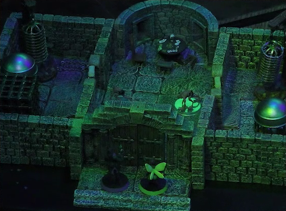 A battlemap of a stone aviary split into three rooms. Occtis and Thimble stand outside a closed door into the main chamber, in which are two ghouls and a circular table with a card game abandoned on it. To the left of the main chamber is a closed door leading to a room with a large cubic black metal cage, a large cylindrical silvery metal cage, and a large cylindrical metal hanging cage resembling a bird cage. To the right of the main chamber is a closed door leading to a room with the same kind of silvery metal cage and hanging cage, although there is no large cubic cage.