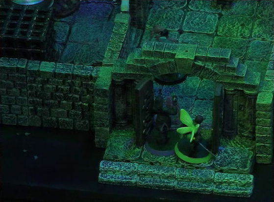 A battlemap of a stone aviary focused on Occtis and Thimble at the open door to a main chamber. Inside the chamber Occtis’s undead monitor lizard faces off against a ghoul. To the left of the chamber is another room with a large cubic black metal cage.