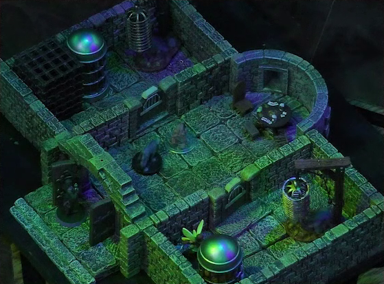 A battlemap of a stone aviary split into three rooms. Occtis stands in the open door to the main chamber, facing off against a ghoul. Inside the main chamber Occtis’s undead monitor lizard faces another ghoul. Thimble is in a room to the right of the main chamber in front of a large cylindrical silvery metal cage. At the rear of the main chamber is a circular table with a card game abandoned on it. To the left of the main chamber is a closed door leading to a room with a large cubic black metal cage, a large cylindrical silvery metal cage, and a large cylindrical metal hanging cage resembling a bird cage. To the right of the main chamber is a closed door leading to a room with the same kind of silvery metal cage, with Thimble in front of it, and hanging cage, although there is no large cubic cage.
