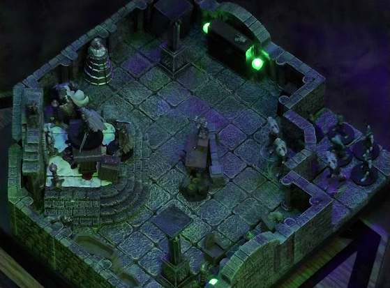 A battlemap of a stone crypt. Teor and Talcydimir stand next to a wooden table on which an undead Raimond Davinos is standing. A hoard of eight zombies enters the crypt from across the room from the table. Two are in the room, the other six are just outside. Teor is positioned on the opposite side of the table from Talcydimir, flanking Raimond. The table sits on a raised part of the floor in front of a wall decorated with carved skull motifs. On a box in front of the table sits a tray bearing multiple surgical instruments. The room is lit by eerie glowing green torches.